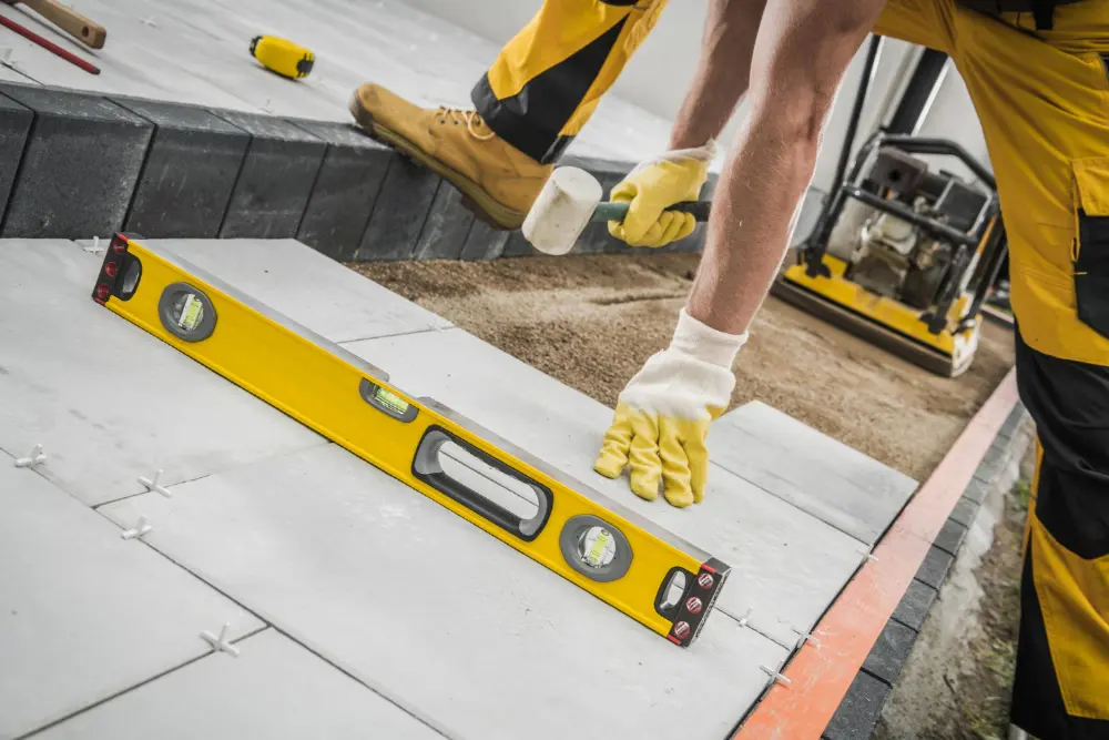 A man in yellow overalls uses a level to measure a floor.