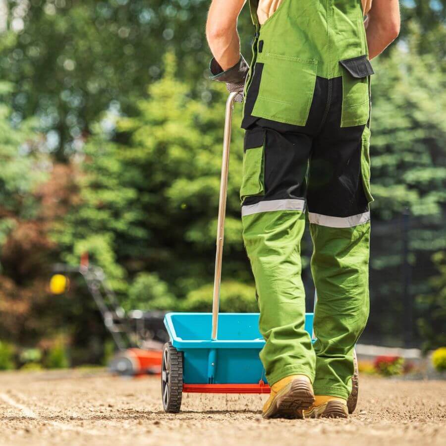 A man in overalls walking with a fertiliser in a garden.