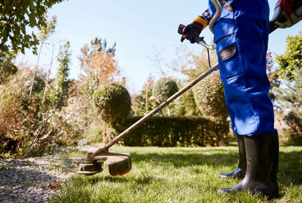 A person in blue overalls mowing the lawn with a lawn mower.